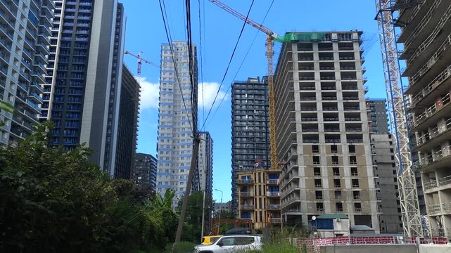Camera pans across high-rise construction in Batumi, Georgia, showing occupied apartment blocks beside unfinished concrete towers, cranes and overhead cables for reports on housing supply