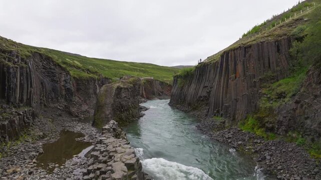 Aerial drone flight inside Studlagil Canyon moving past massive geometric basalt columns over glacial river in Iceland