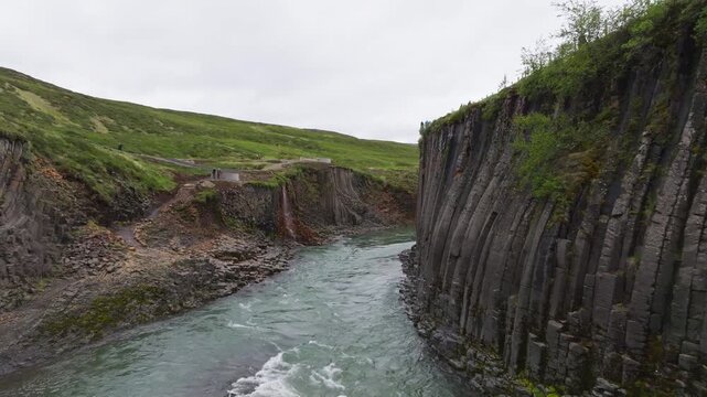 Aerial drone flight inside Studlagil Canyon moving past massive geometric basalt columns over glacial river in Iceland