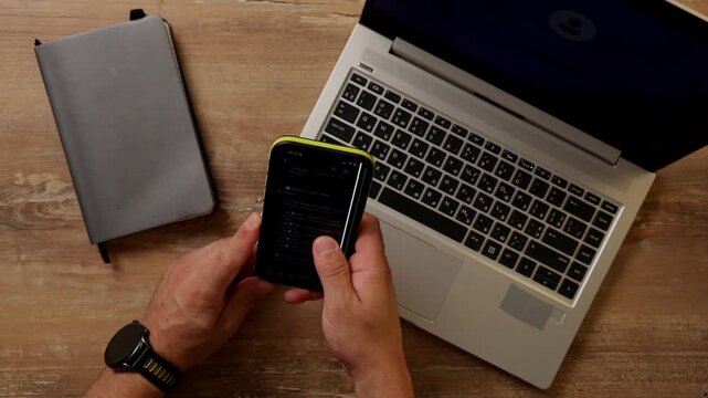 Hand scrolls on smartphone and places it next to a notebook on a table