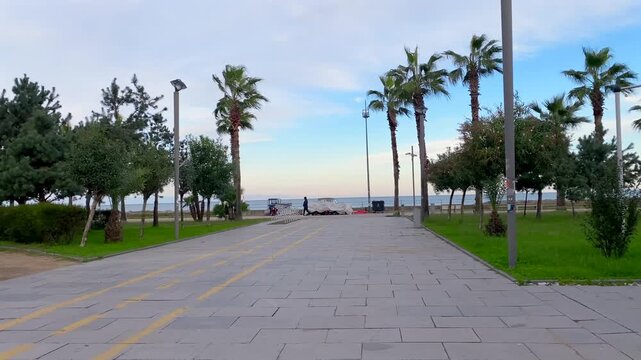 A paved promenade lined with palms leads toward the Black Sea as pedestrians cross the frame. This waterfront view suits public infrastructure presentations, tourism campaigns and planning media