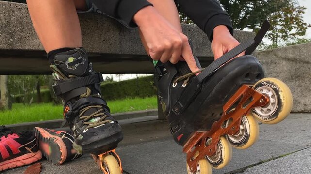 A skater adjusts the buckles and laces on inline boots before a ride, showing a hands-on gear check. Useful for skating safety guides, sporting goods promotions and beginner training materials.