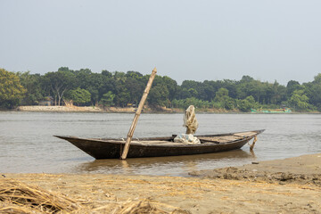 Small wooden dinghy boat moored along a sandy river shore in South Asia. Scenic countryside river landscape with lush green bank background. © Sahadat