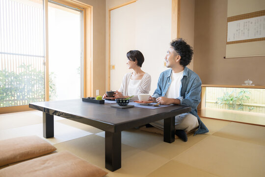 温泉旅館の和室で窓の外の美しい景色を眺めながら旅行を楽しむ日本人夫婦、観光旅行や国内旅行の宿泊先イメージ