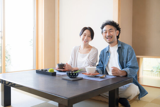 温泉旅館の和室でくつろぐ旅行を楽しむ日本人夫婦、観光旅行や国内旅行の宿泊先イメージカメラ目線笑顔