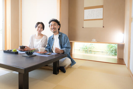 温泉旅館の和室でくつろぐ旅行を楽しむ日本人夫婦、観光旅行や国内旅行の宿泊先イメージカメラ目線笑顔全身の広角