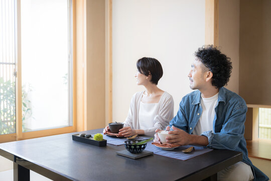 温泉旅館の和室で窓の外の美しい景色を眺めながら旅行を楽しむ日本人夫婦、観光旅行や国内旅行の宿泊先イメージ