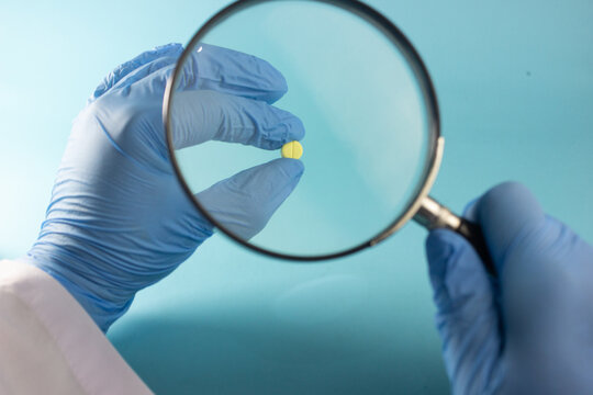 gloved medical hand holding pill with a magnifying glass, symbolizing pharmaceutical research, drug inspection, medication safety, illegal drugs medical malpractice, drug misuse healthcare regulation