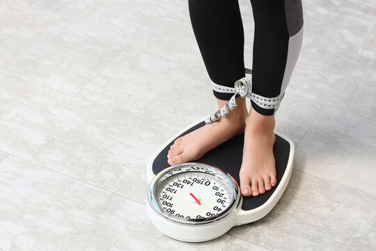 Weight loss and body image struggle, woman standing on a scale with measuring tape tied around her ankles obsession with body weight