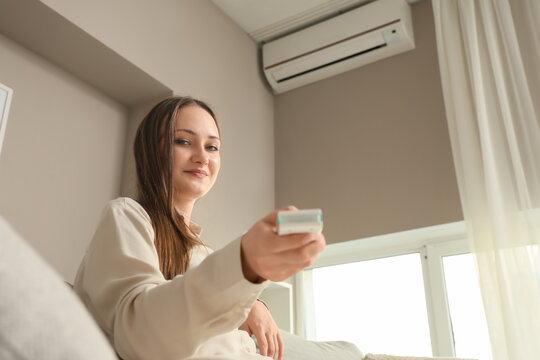 Climate control and energy efficiency, woman using air conditioner remote at home to adjust room temperature for comfort and cooling during summer heat