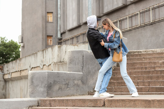 Street harassment and personal safety, young woman defending herself from an aggressive stranger on urban stairs in a city environment
