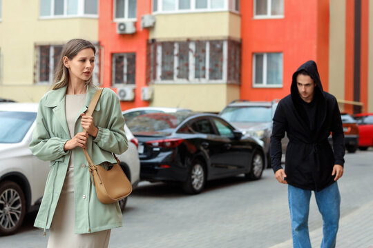 Personal safety and street harassment, woman feeling anxious while being followed by a suspicious man in a hoodie on a city street