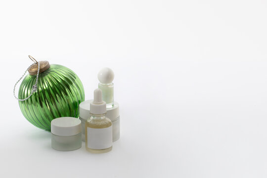 Luxury winter skincare collection featuring frosted glass bottles and a decorative green ornament. Suitable for boutique Christmas catalogs, high-end beauty marketing, and festive skincare gifting.