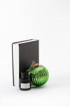 Festive gift for man black perfume bottle stands alongside a festive green glass ornament and a dark book. Excellent for holiday bundle deals and skincare gift guide visuals.