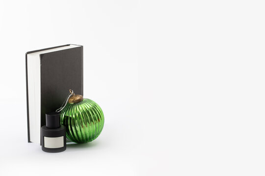 A sleek black perfume bottle stands alongside a festive green glass ornament and a dark book. Perfect for sophisticated holiday gifting, luxury fragrance deals, and seasonal editorial layouts.
