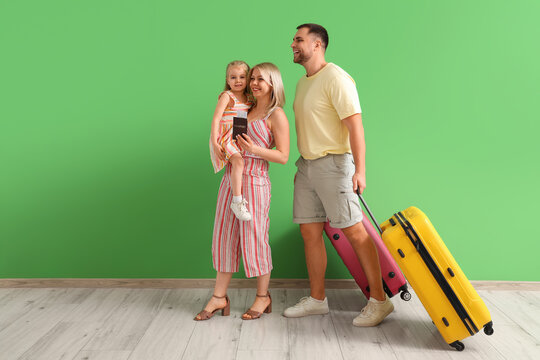Family travel and vacation planning, happy parents with daughter holding passport and luggage ready for summer holiday trip against green background