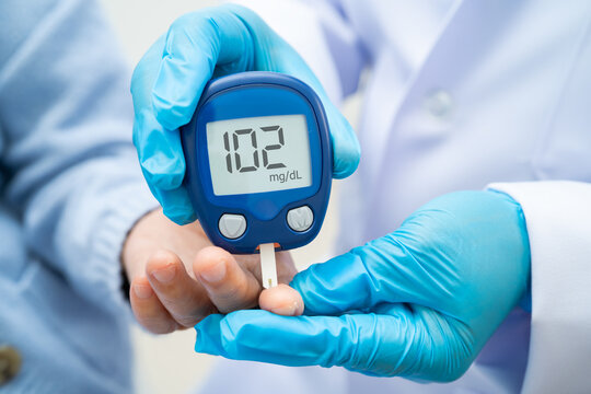 Asian doctor using digital glucose meter for check sample blood sugar level to treatment diabetes.
