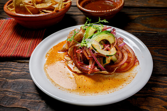 Red aguachile tostada with red onion, avocado and cucumber in chili sauce