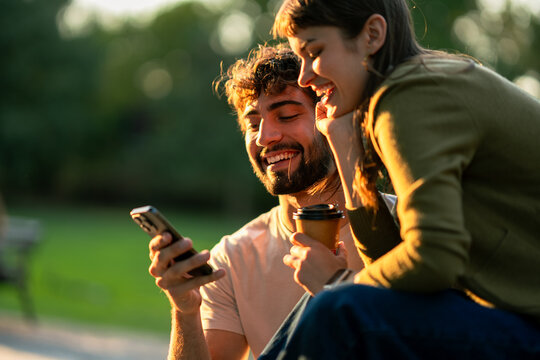 Young couple laughing while looking at a mobile phone during golden hour