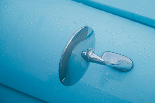 Close up of vintage blue car fender mirror covered in fresh raindrops.
A high-quality close-up photograph capturing the classic chrome round fender mirror of a vintage retro automobile. The glossy