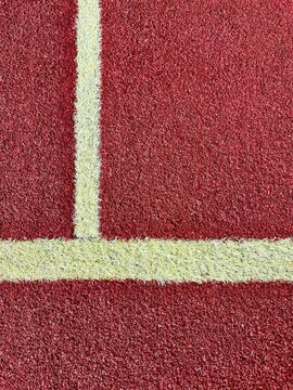 Overhead close up of white T junction line on red synthetic grass court, abstract sport surface background