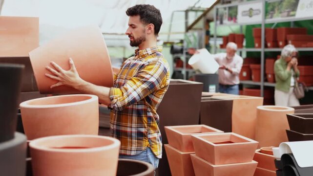Man in garden goods store carefully chooses flower pot, studies assortment, admires variations ceramic or plastic products. Concept of self-decoration of housing, indoor plants 