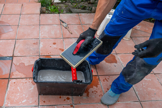Worker applying grout on tiled floor with hand tools outdoors