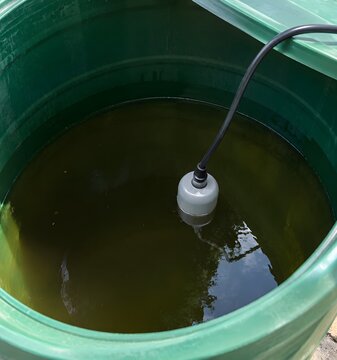 Water barrel with float level sensor inside and cylindrical float bobbing on dark water inside a green plastic tank