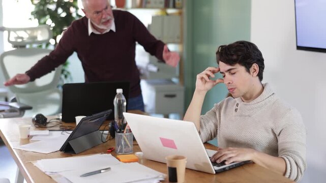 Senior man head of department shouts at guy subordinate who is working at laptop. Toxic relationships at work, reproaches and claims, violation of personal boundaries 