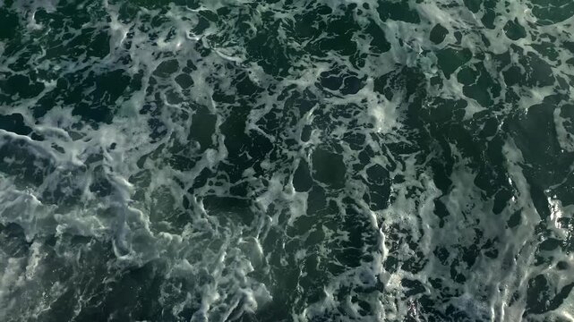 Green tinted water churns with white foam along the coast, documenting wave turbulence for storm impact monitoring, marine condition reports and environmental risk assessment for coastal authorities