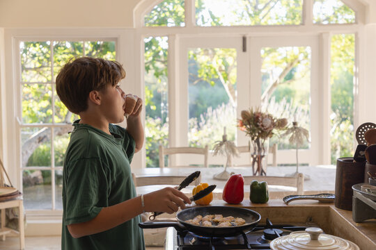early teen boy panfrying chicken strip in light filled kitchen