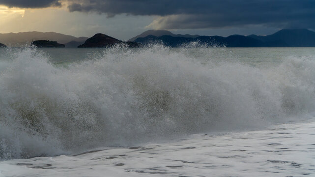 Fethiye, Turkey, stormy Mediterranean Sea with a big wave crashing onto the beach, sea spray and dark storm clouds over the islands of the coast