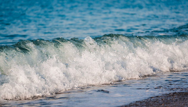 Breaking sea wave rolls toward shore with white foam and dynamic coastal energy