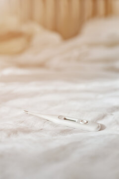 Digital thermometer lying on a white bed sheet in a bedroom