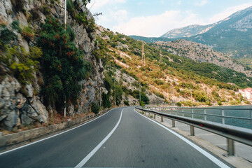 Naklejka premium Curved road along rocky mountainside near water in daylight