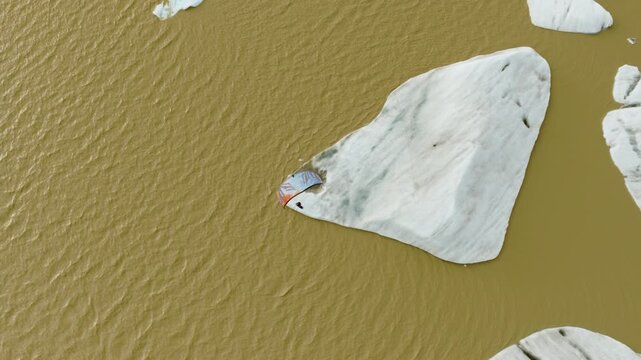 Kitesurfer crosses Fjallsarlon Glacier Lagoon, Hornafjordur, South Iceland, Iceland, beside a massive floating ice formation, top down drone tracking