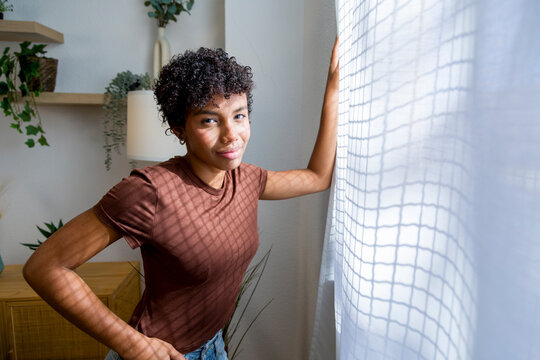 Young African American woman standing by window inside home interior