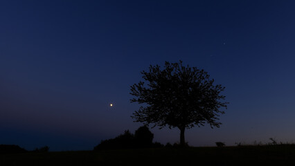 Fototapeta premium Moon on a twilight sky with stars, planets and landscape mountain silhouettes.