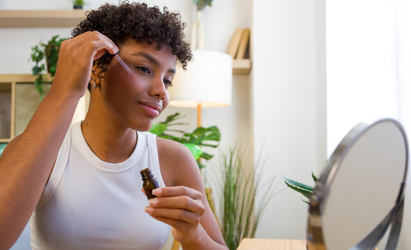 African American woman applying face serum with dropper