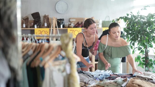 Two young women carefully choosing fashionable jeans or shorts in a clothing store . High quality 4k footage