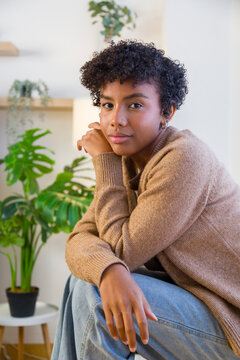 Young African American woman posing indoors by a monstera plant