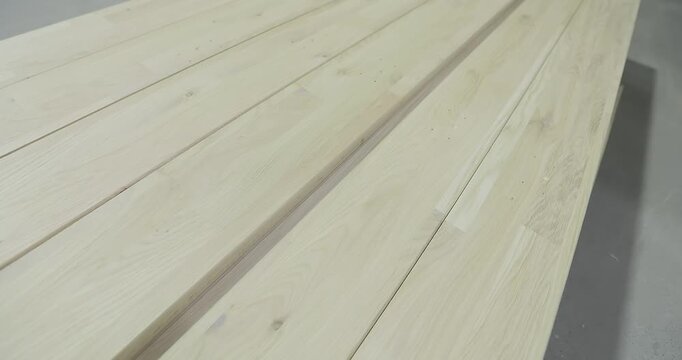 Light-colored long lumber with a wood texture is prepared for further processing. A stack of edge-glued panels or a furniture panel for woodworking on the floor of a furniture factory workshop.