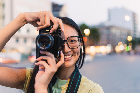 Smiling woman takes a picture with a camera on an urban street