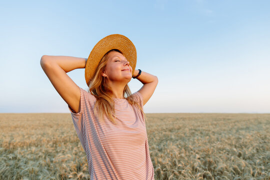 Smiling woman relaxes in a wheat field at sunset enjoying inner peace