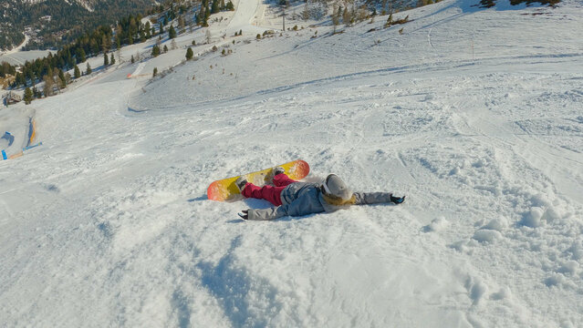 Girl snowboarder falls back on snow while learning to snowboard on ski slope