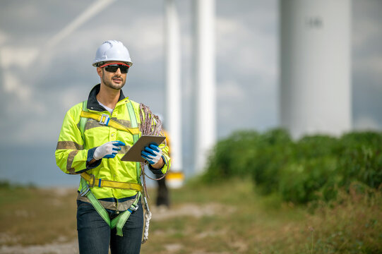 Industrial engineer inspecting wind turbine power generator sustainability performance inspection at Renewable Energy Plant Male worker wearing safety suit and hardhat using tablet at windmill