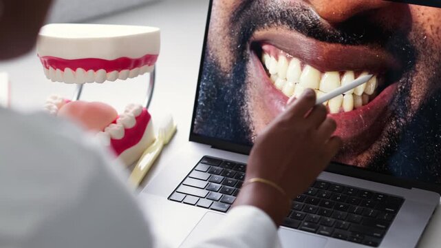 African female dentist examining a patient&rsquo;s teeth on a laptop screen, pointing at dental concerns
