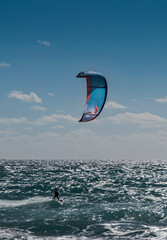 Lone kitesurfer riding the waves off Tarifa, Spain, beneath a large kite silhouetted against a bright sky and sparkling sea, capturing freedom, wind and open space © ihervas