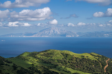 View across the Strait of Gibraltar from Mirador del Estrecho, Spain, towards the mountains of Morocco. Rolling green hills, deep blue sea and scattered clouds under clear daylight © ihervas
