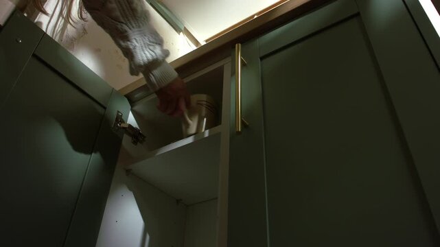 Hand getting mug for coffee out of kitchen cabinet shelf
